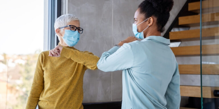 Senior Woman and Nursing Staff Wearing Masks Greeting Each Other at a Memory Care Facility